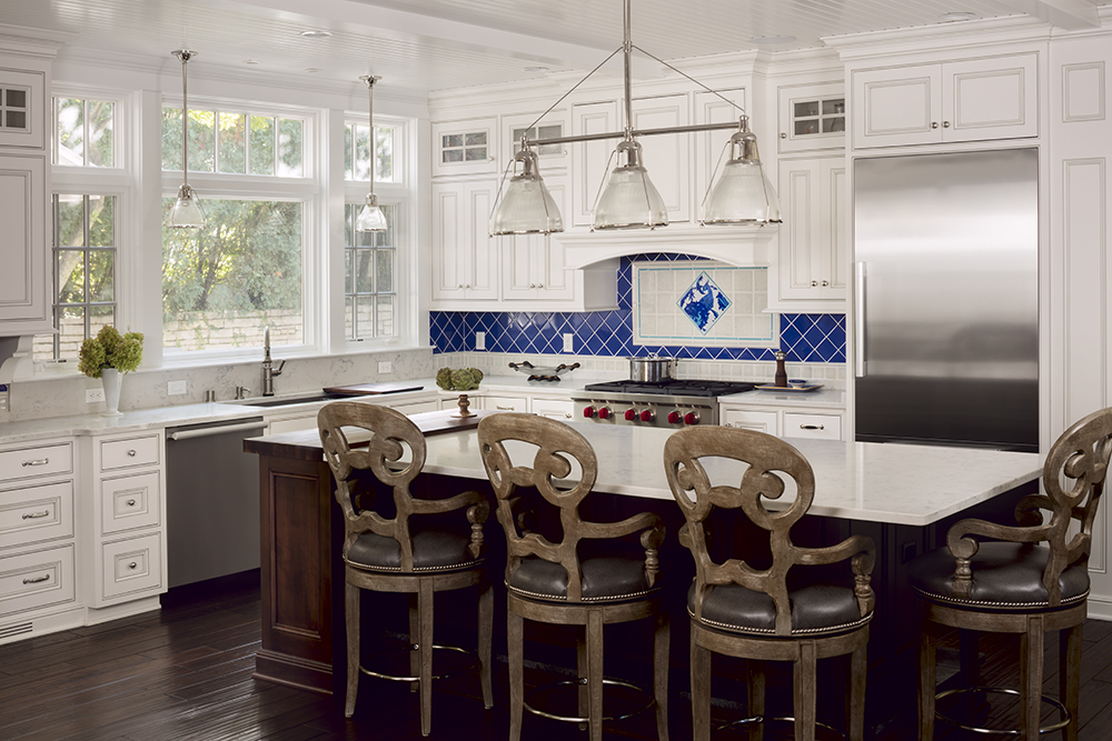 large kitchen with white cabinetry, brown wood floors and chairs, royal blue back splash and white island