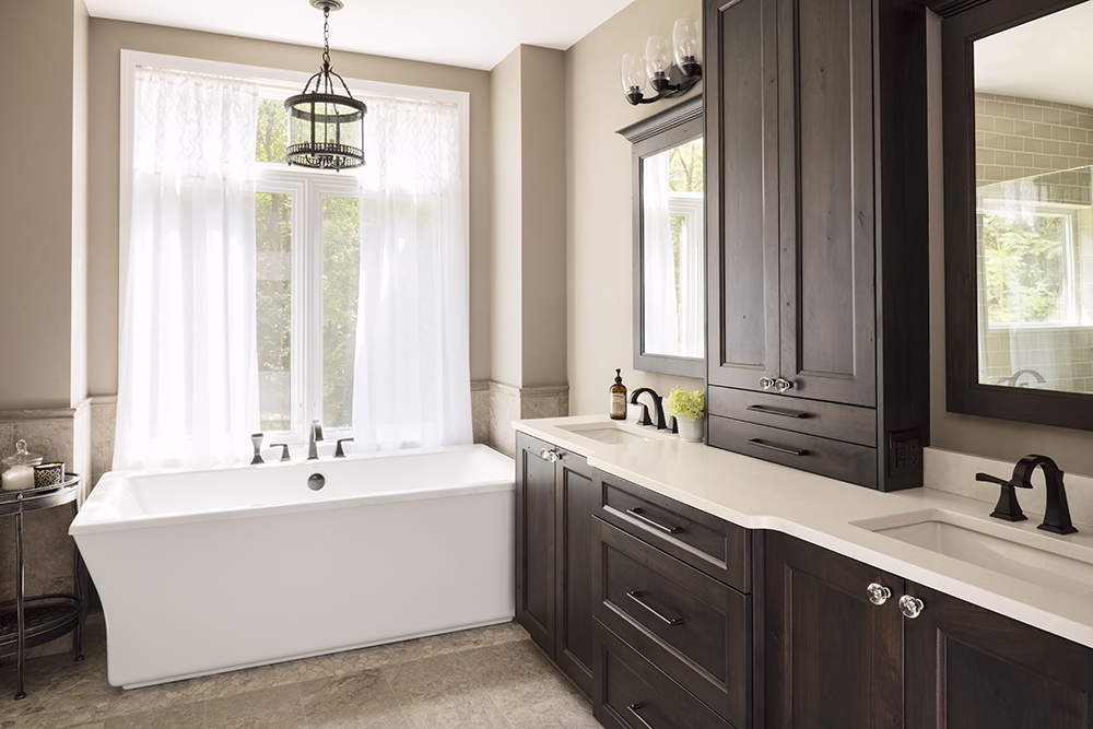 bathroom with dark wood cabinetry, dual vanities, and white tub in front of large window